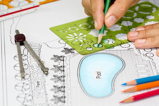 Une personne dessine sur un plan d'aménagement paysager avec un crayon vert, coloriant une zone végétalisée